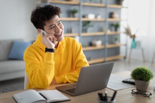 Cheerful asian man working and talking on cellphone using pc